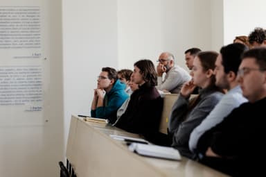 Studentai sėdi auditorijoje ir susidomėję klausosi